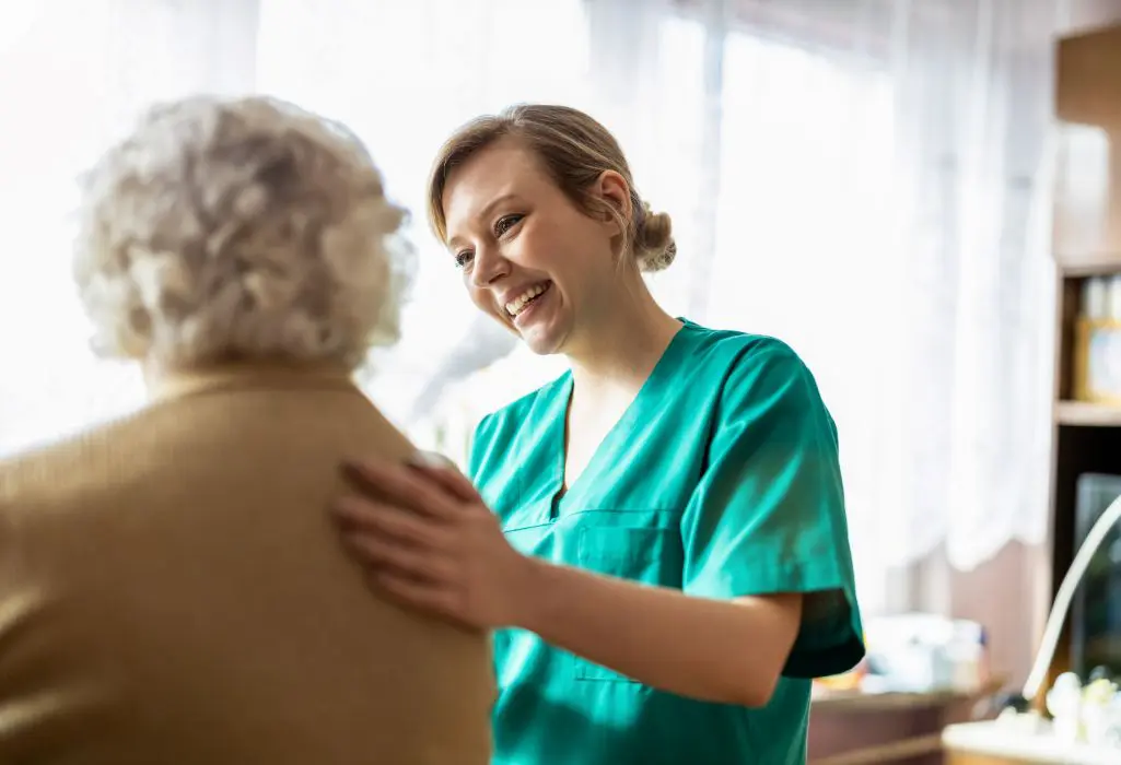 A nurse is smiling as she holds the arm of an older woman.