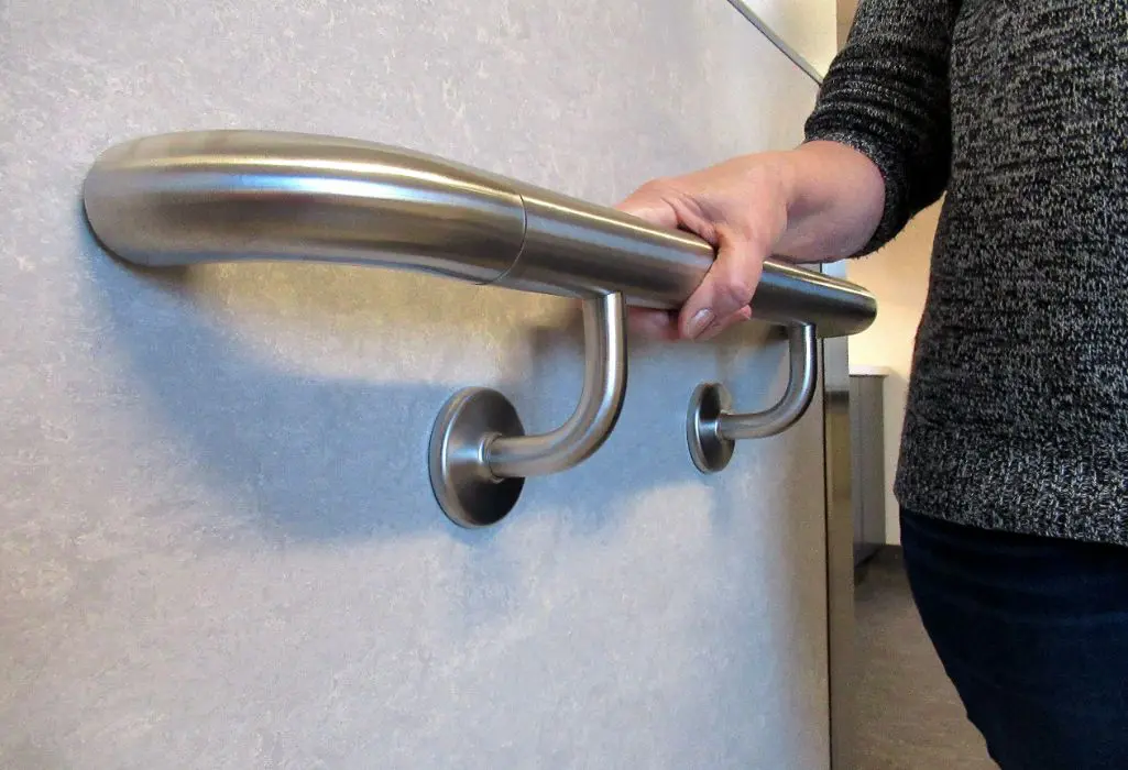 A person holding onto the handrail of a bathroom.